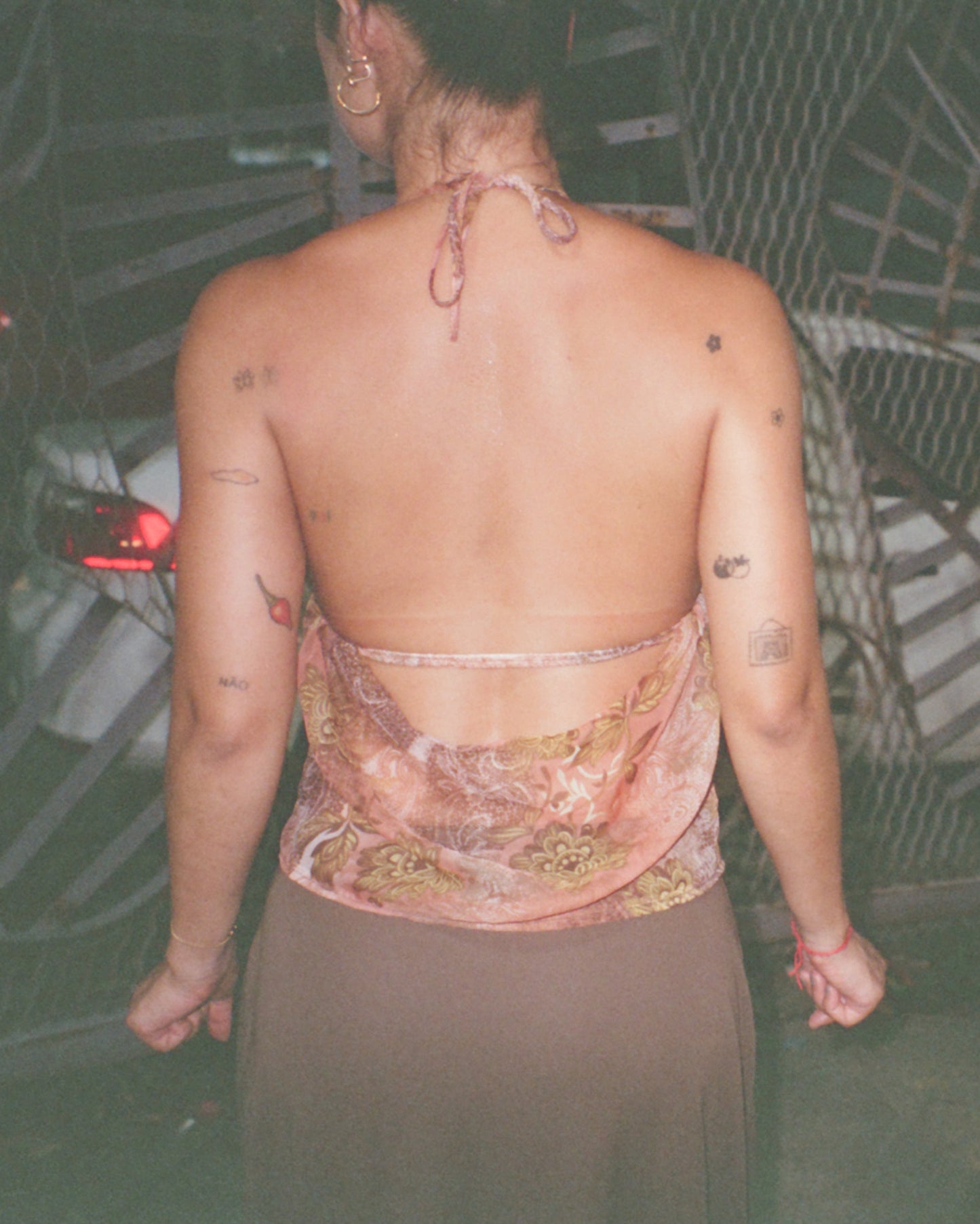Person wearing a patterned caju.nyc top with tattoos visible on their back, standing in front of a textured wall.