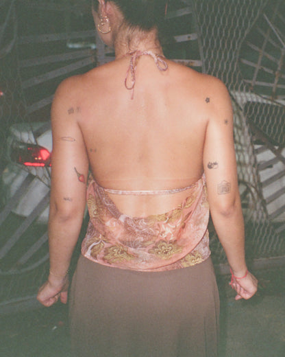 Person wearing a patterned caju.nyc top with tattoos visible on their back, standing in front of a textured wall.