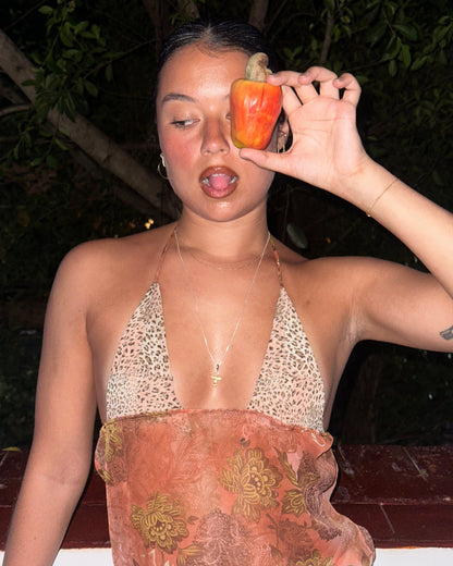 Person holding a caju fruit near their face in a windowsill wearing a caju.nyc tank top inspired by roberto cavalli