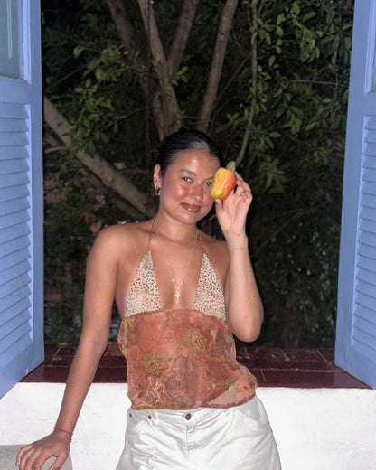 Person holding a caju fruit near their face in a windowsill wearing a caju.nyc tank top inspired by roberto cavalli
